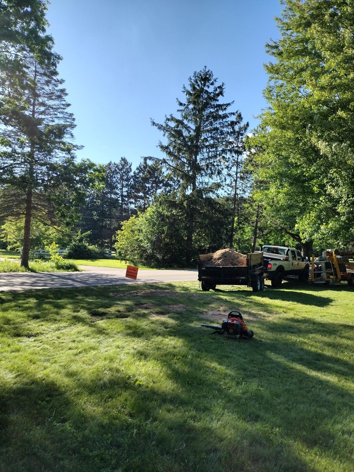 A sunny park scene; truck loaded with debris, equipment, a person, and lush green trees.