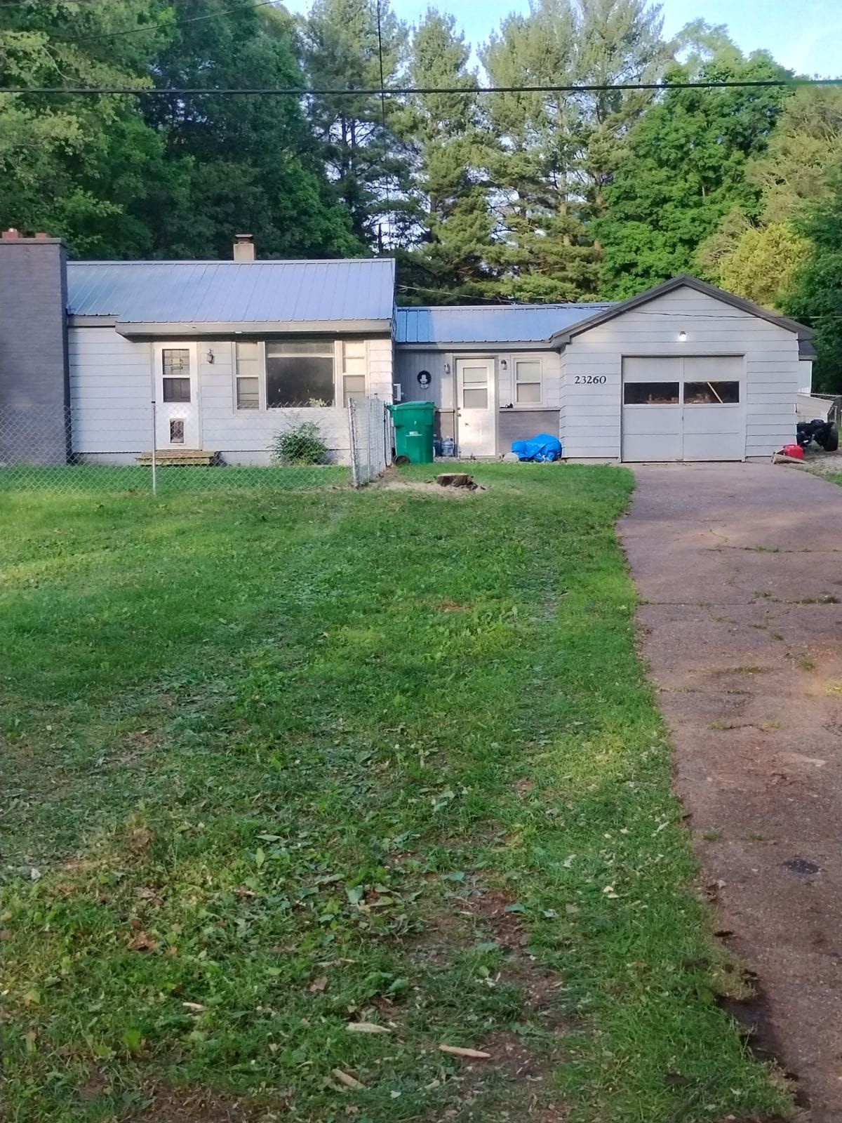 Gray house with a green lawn and a concrete driveway. Garage door is closed. Trees are in the background.