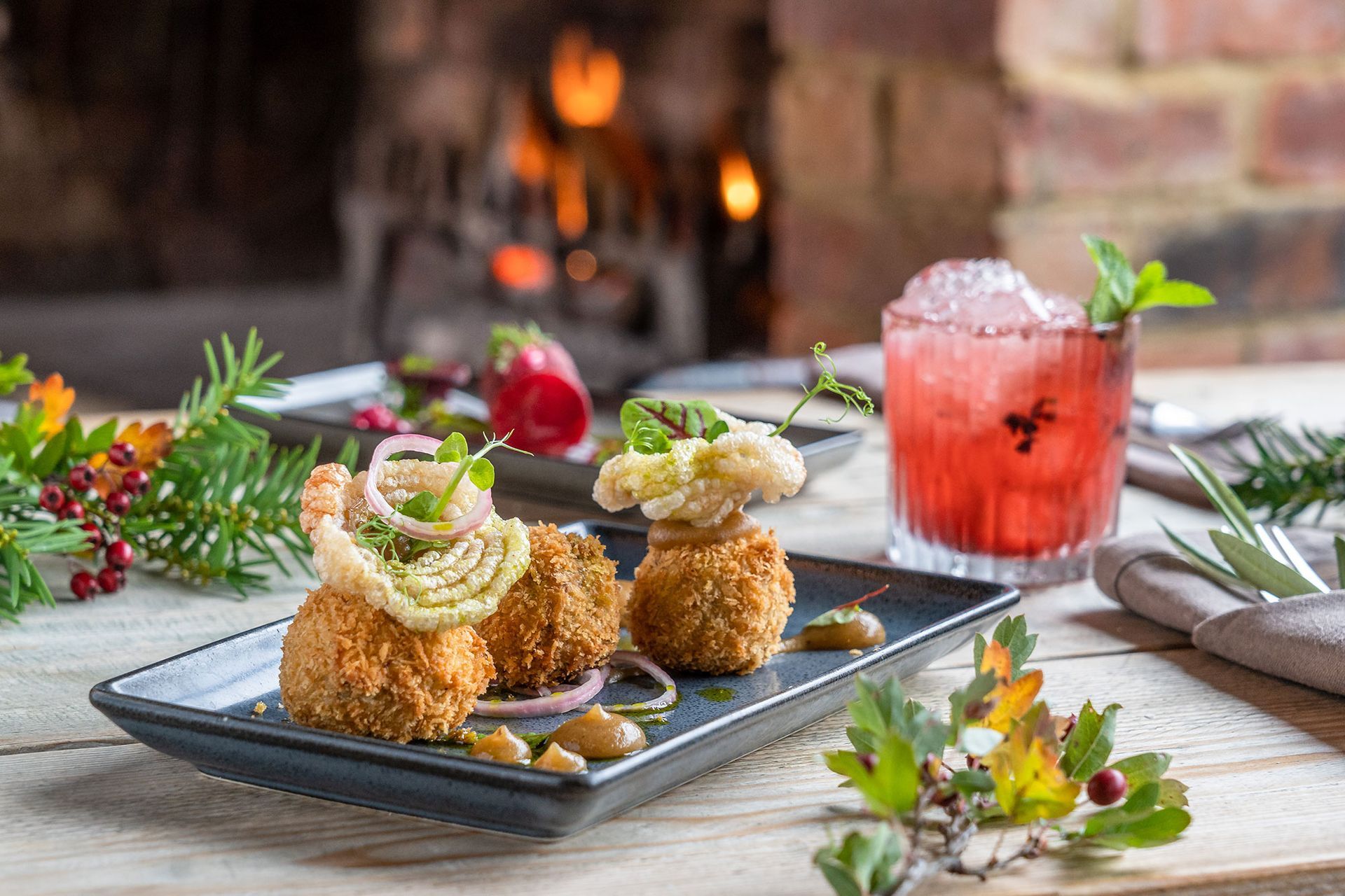 Appetizers with a cocktail on a table with a fireplace in the background.