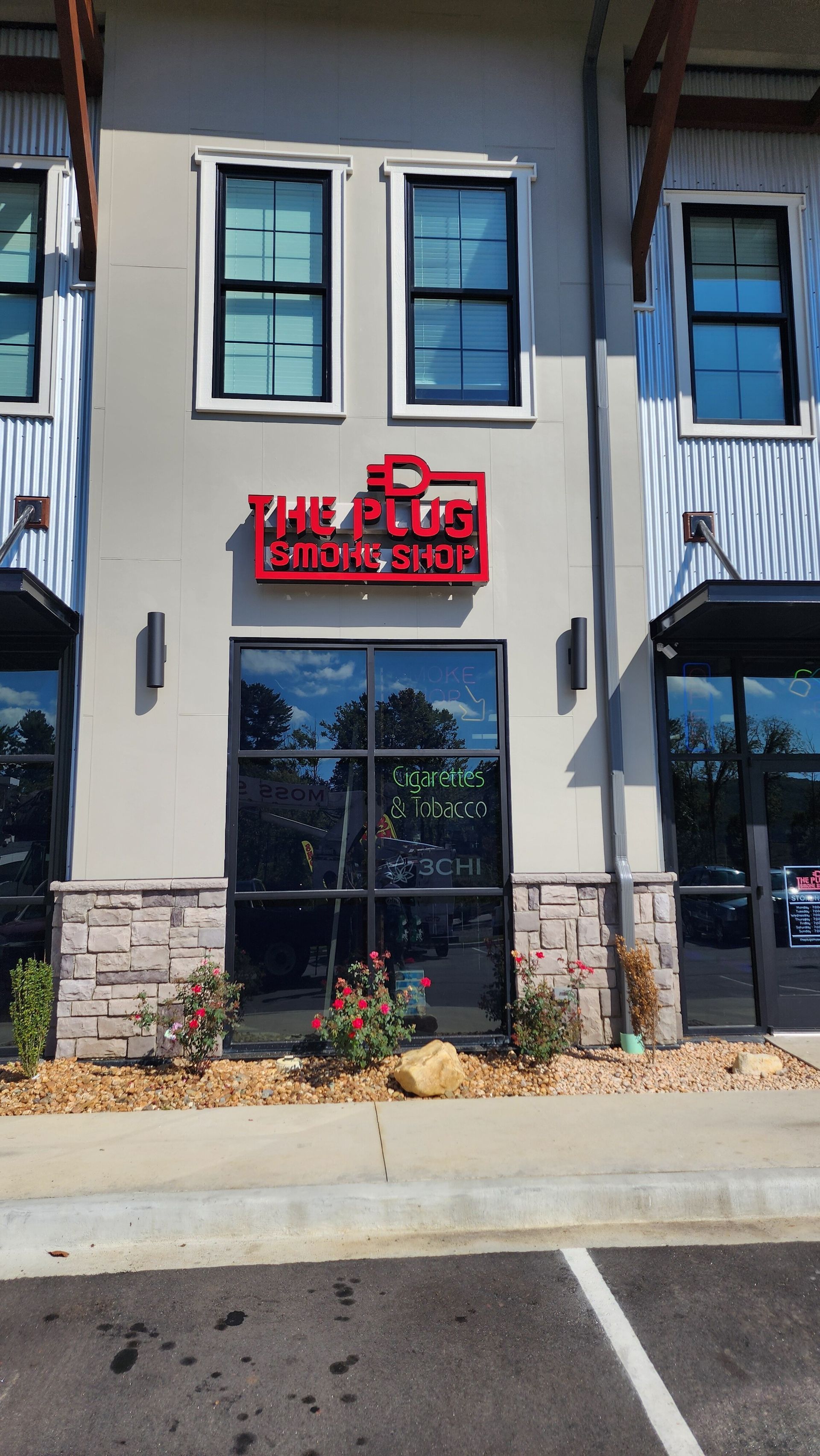 Exterior of The Club Car Wash, a red and black sign above a glass door, with flowers below and windows above.