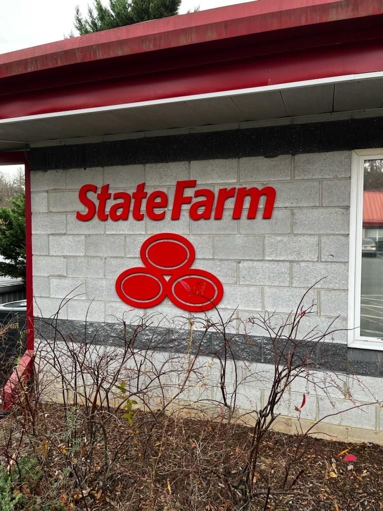 State Farm sign in red on a gray brick building with a red awning; shrubs are in front.