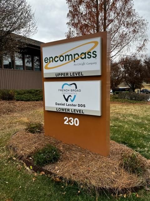Sign for Encompass and French Broad Dental EDS at 230. Brown rectangular sign with white and colored logos, surrounded by mulch and greenery.