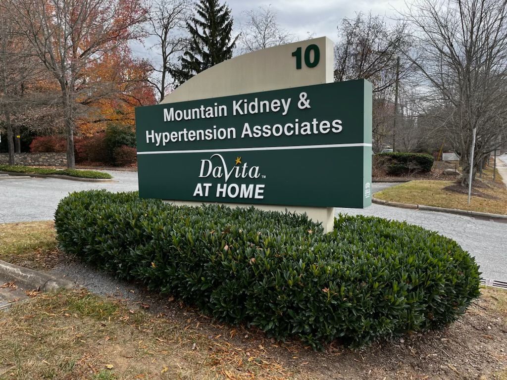 Sign for Mountain Kidney & Hypertension Associates, a DaVita location. Features green and beige panels with building number 10, and a hedge in front.