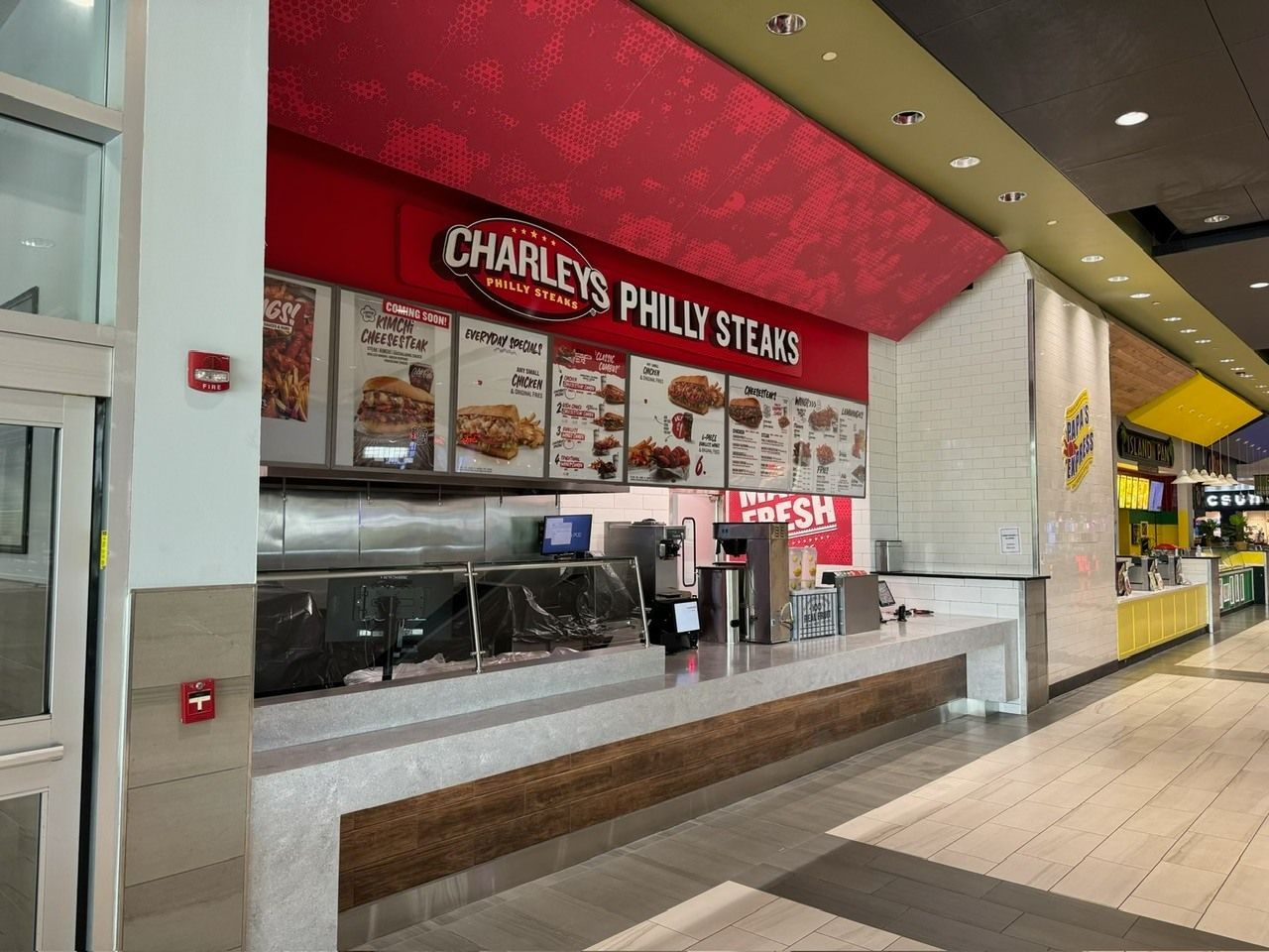 Charleys Philly Steaks restaurant at a mall. Red and white signage with menu. Light-colored countertop and stainless steel equipment.