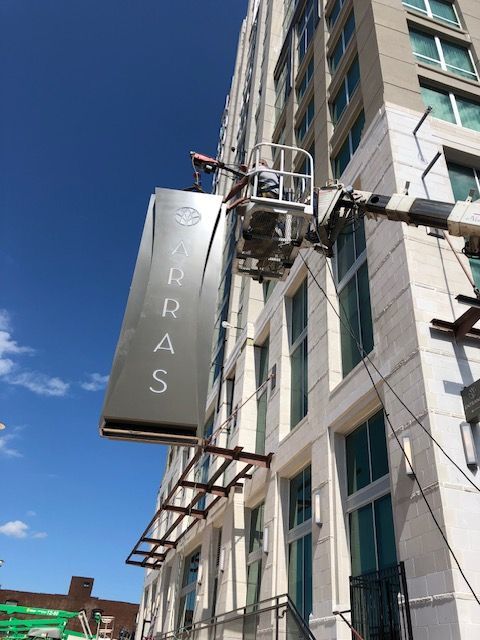 A worker in a lift installs a large silver sign for 