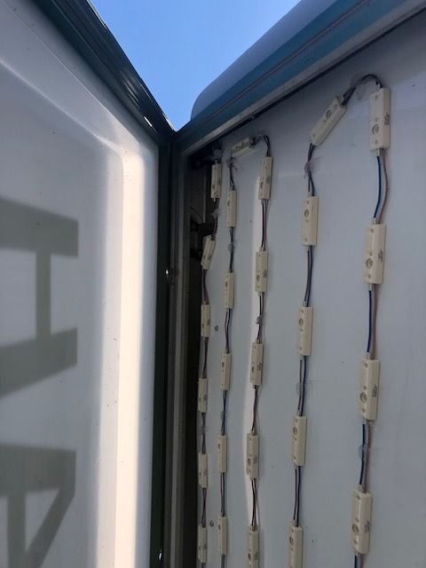 Inside of a sign with a row of white LED lights attached to a white surface, wired together.