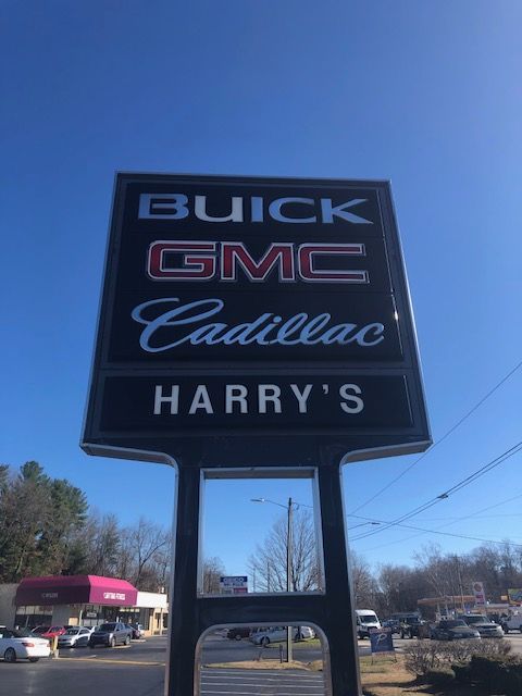 Sign for Harry's Buick GMC Cadillac dealership on a sunny day, showing the brands' logos above the business name.