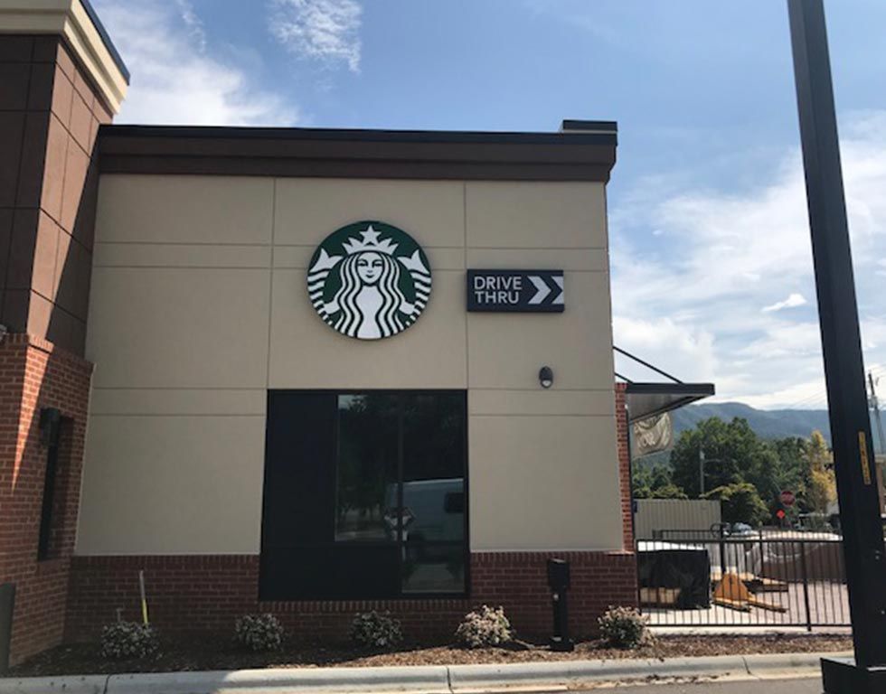 Starbucks building with drive-thru signage. Cream-colored walls, a green and white logo, and a brick base under a blue sky.