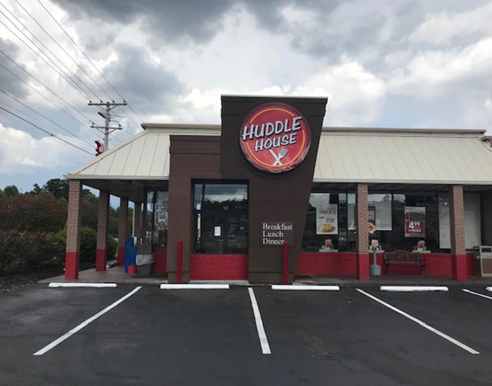 Huddle House restaurant with brown and white exterior and red accents, cloudy sky.