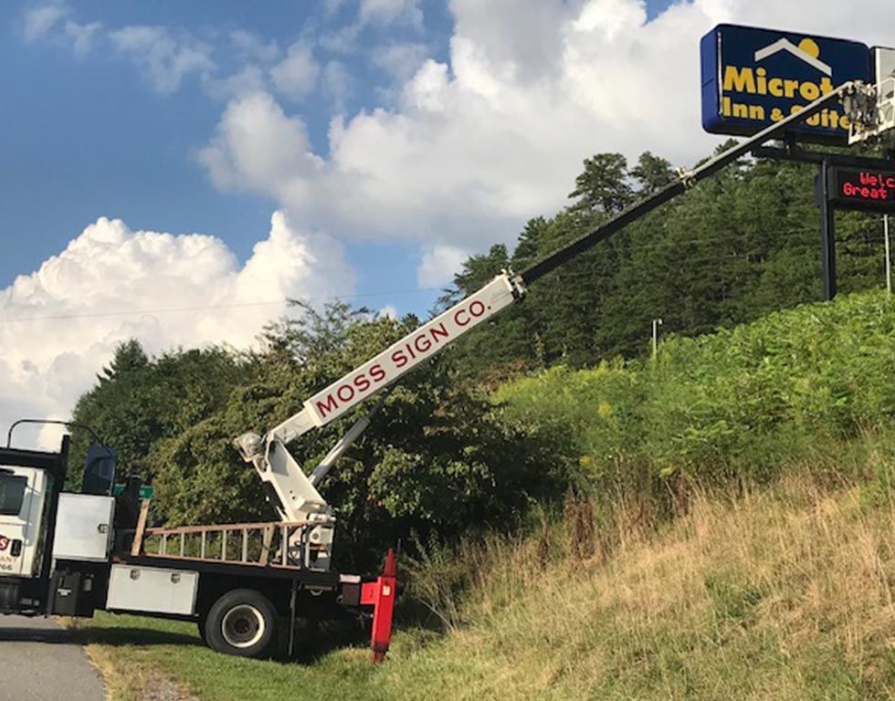 A Moss Sign Co. truck with an extended crane working on a motel sign. The sign reads 