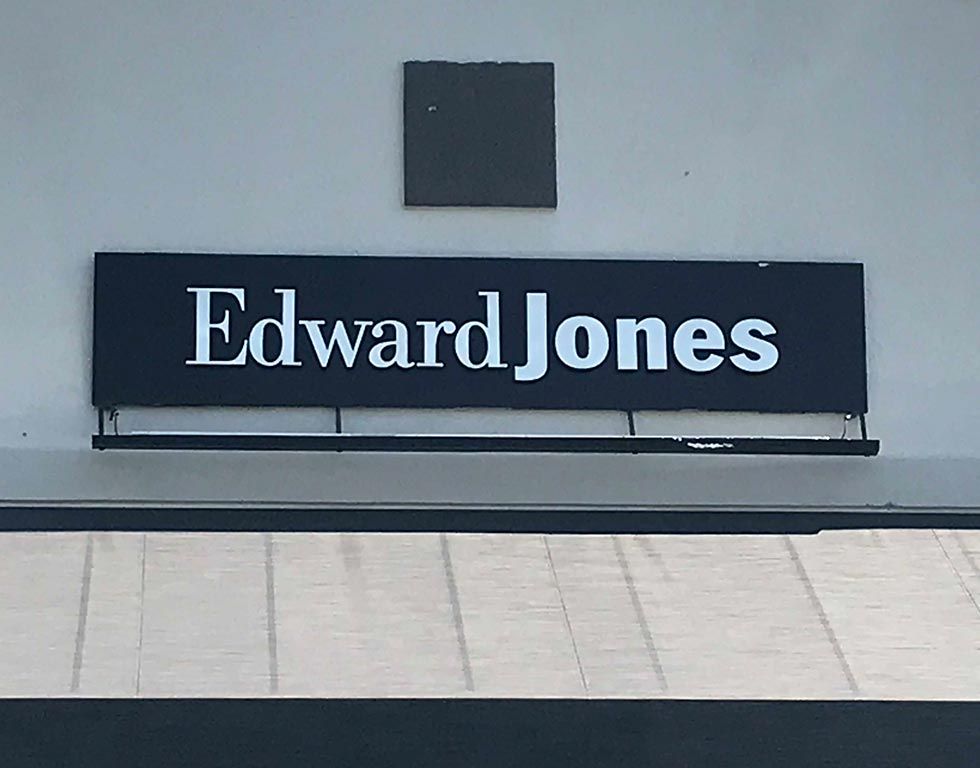 Edward Jones sign in white letters on a black rectangular background, mounted on a light-colored building.