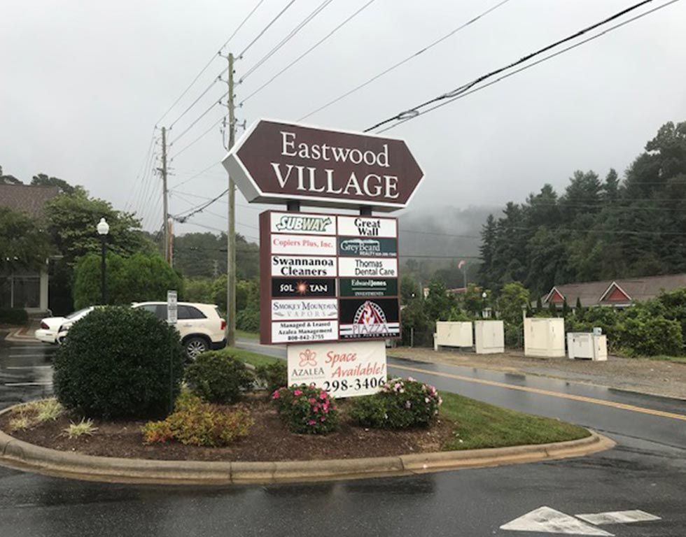 Eastwood Village sign on a cloudy day, featuring business names and 