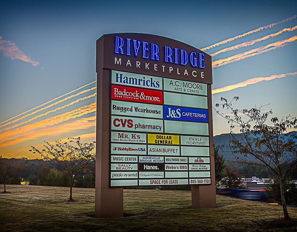 Sign for River Ridge Marketplace at dusk, listing stores: Harris Teeter, CVS, and more. Sky is orange and blue.