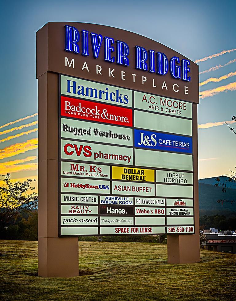 Sign for River Ridge Marketplace, displaying businesses including Hamricks, CVS Pharmacy, and Dollar General, set against a sunset sky.