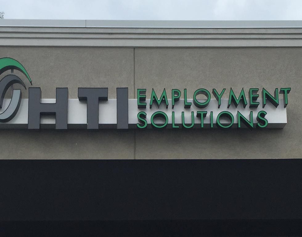 Sign for HTI Employment Solutions in green and black letters on a gray building.
