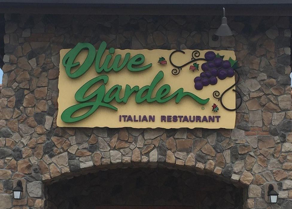 Olive Garden Italian Restaurant sign on a stone facade, green lettering, and a grape vine design.
