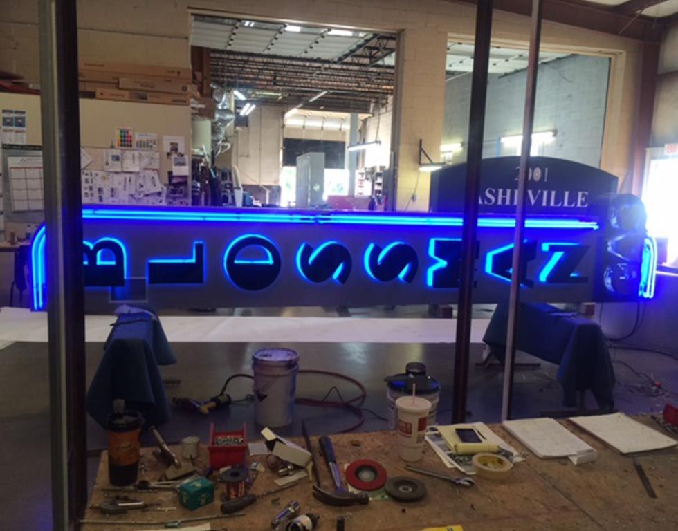 Large illuminated sign being assembled in a workshop. The sign reads 