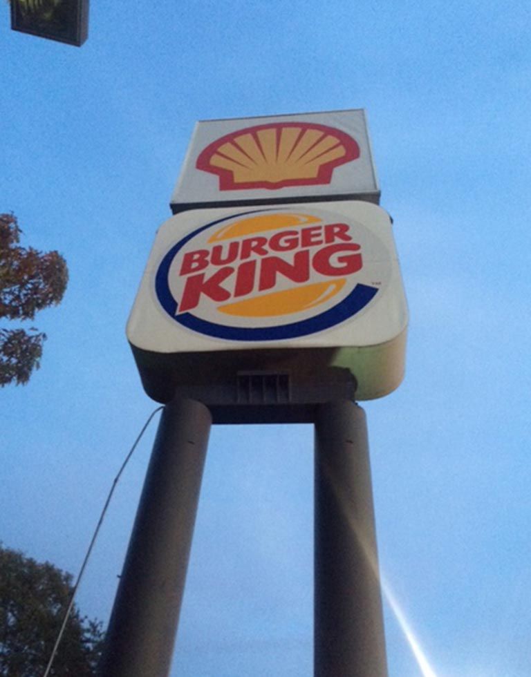 Sign with a Shell logo on top and a Burger King logo below, supported by two columns, against a blue sky.