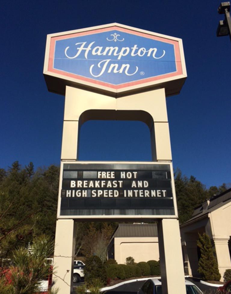 Sign for Hampton Inn hotel: Blue and white logo atop a tall sign, below which advertises free hot breakfast and high-speed internet.