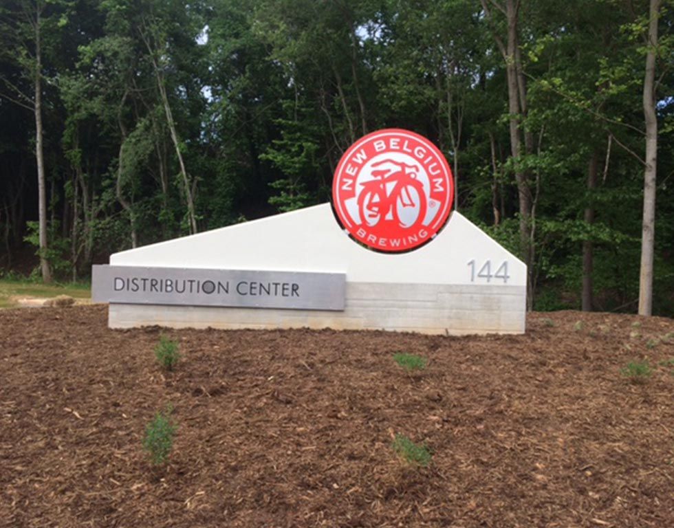 Sign for New Belgium Brewing Distribution Center at 144, with their logo. Gray and red logo on a white sign.