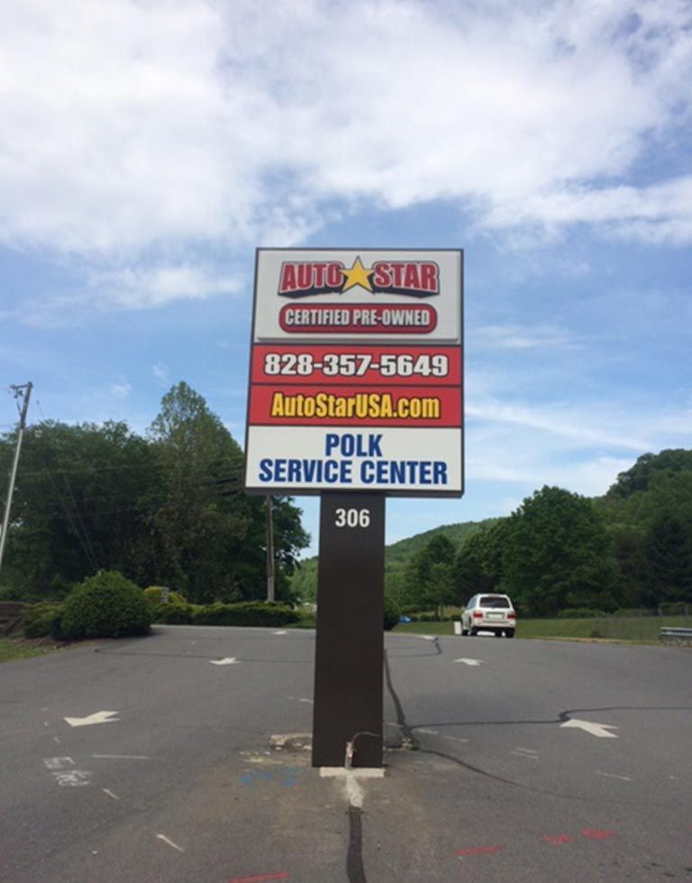Sign for Auto Star certified pre-owned and service center, with phone number and website. Set in front of a road with a vehicle visible.
