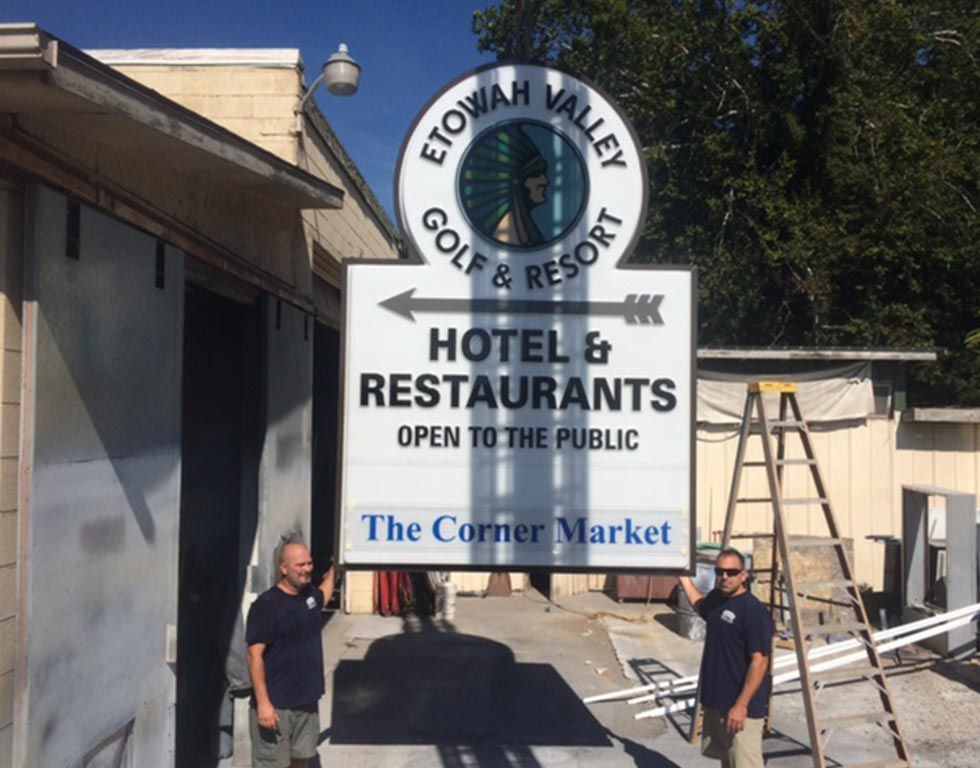 Two men holding a large sign for Etowah Valley Golf & Resort, pointing to a hotel and restaurants. The sign also promotes 