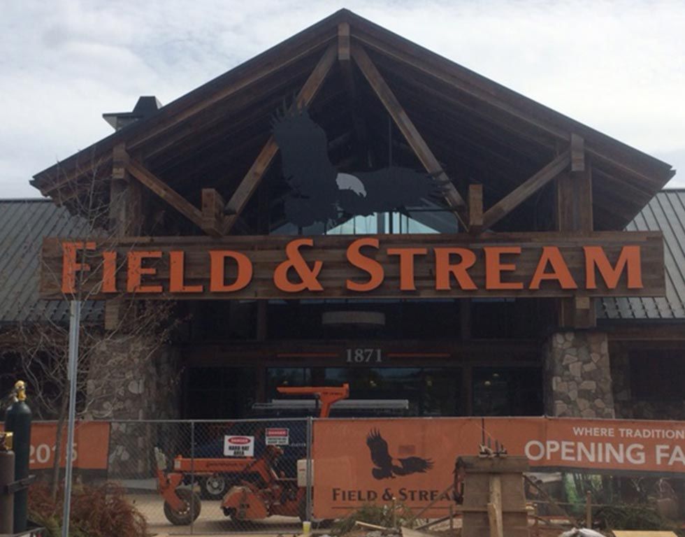 Field & Stream store exterior with brown sign and eagle logo. Construction equipment visible, indicating a grand opening.