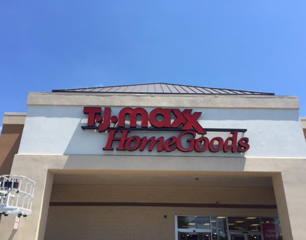 TJ Maxx and HomeGoods store sign in red against a beige building and clear blue sky.