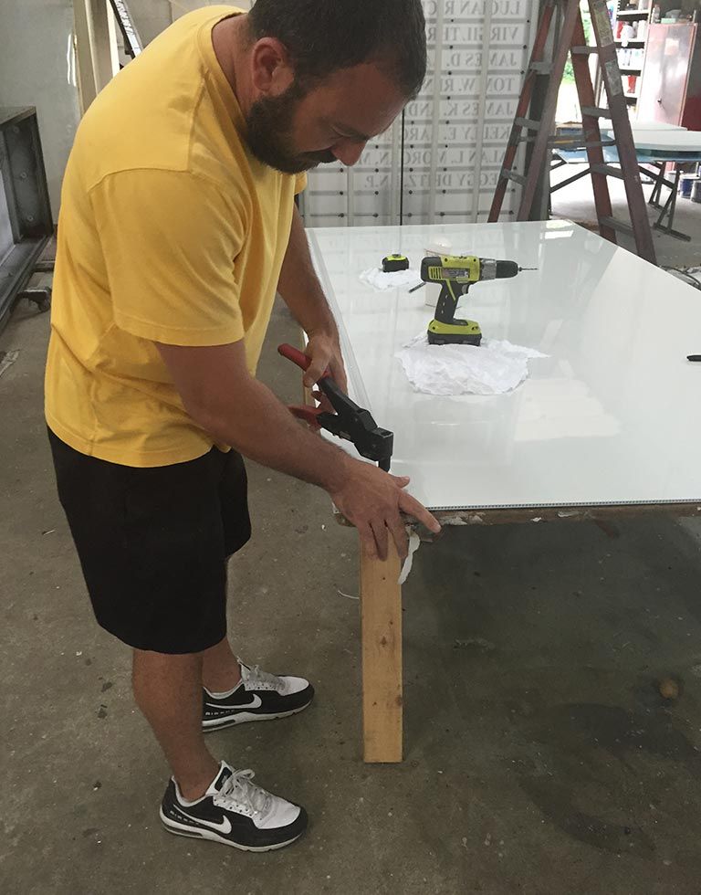 Man in yellow shirt using a tool on a white surface. He's working outdoors near a ladder.