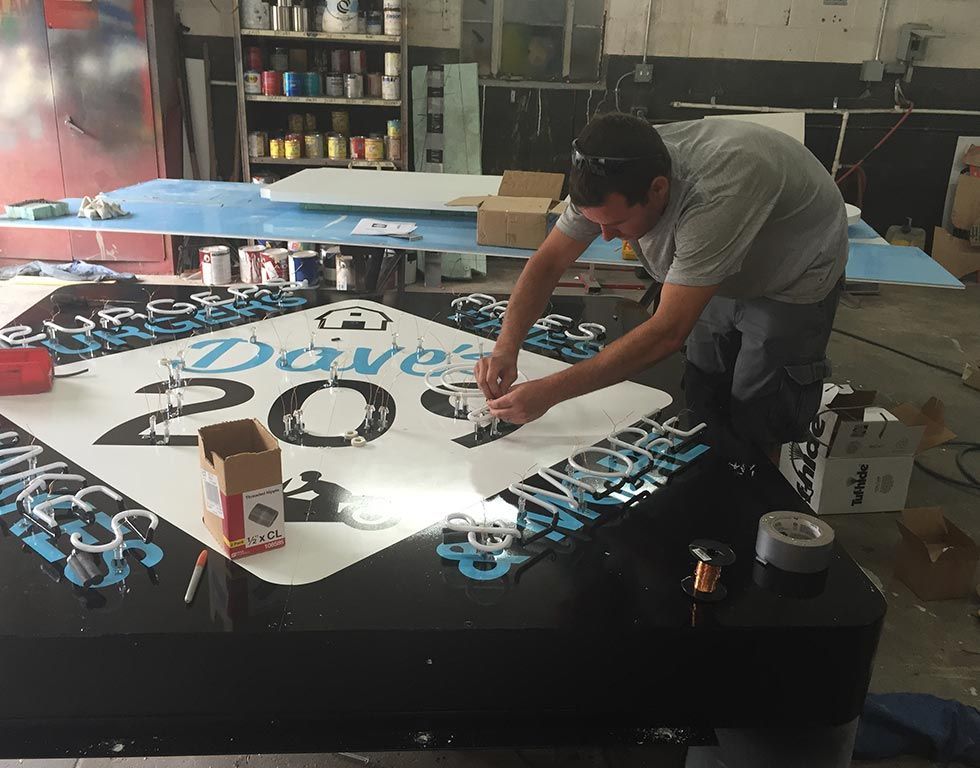 Man working on a large black sign, attaching decorative elements. The sign has white and blue details, likely for a business named 