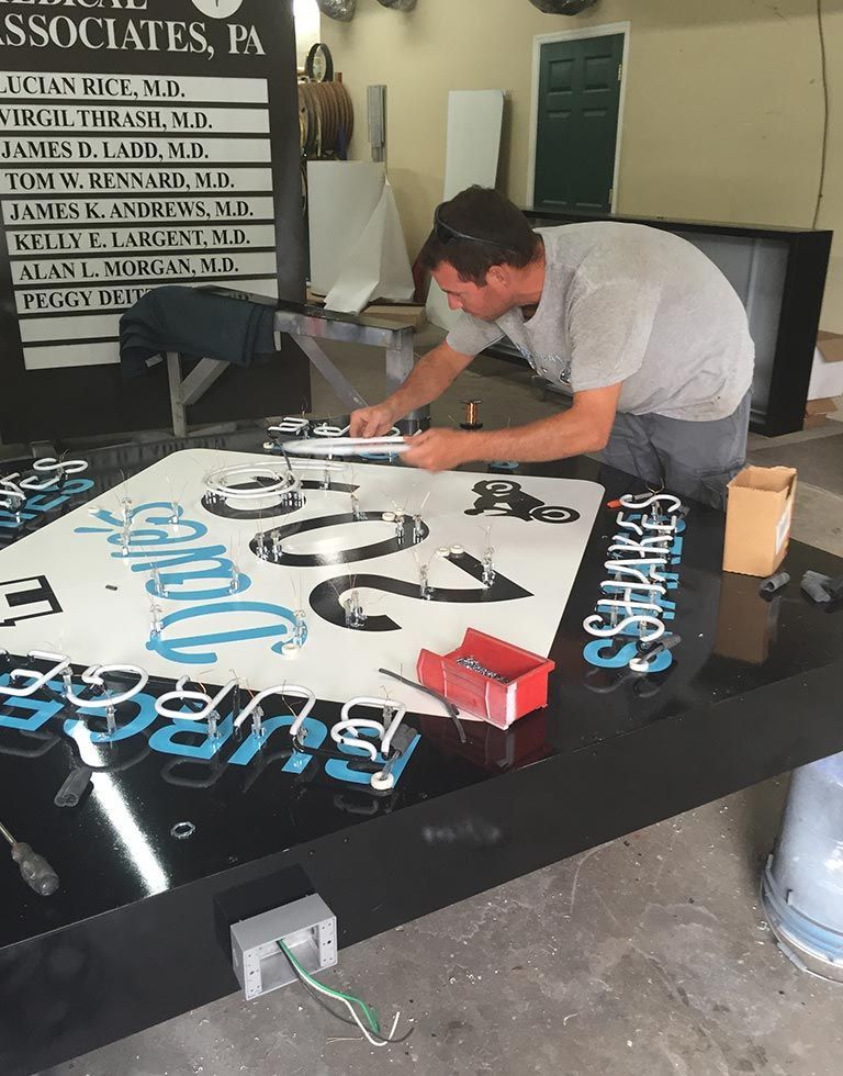 A man working on a large sign, assembling letters and numbers. The sign is black, with white and blue elements.