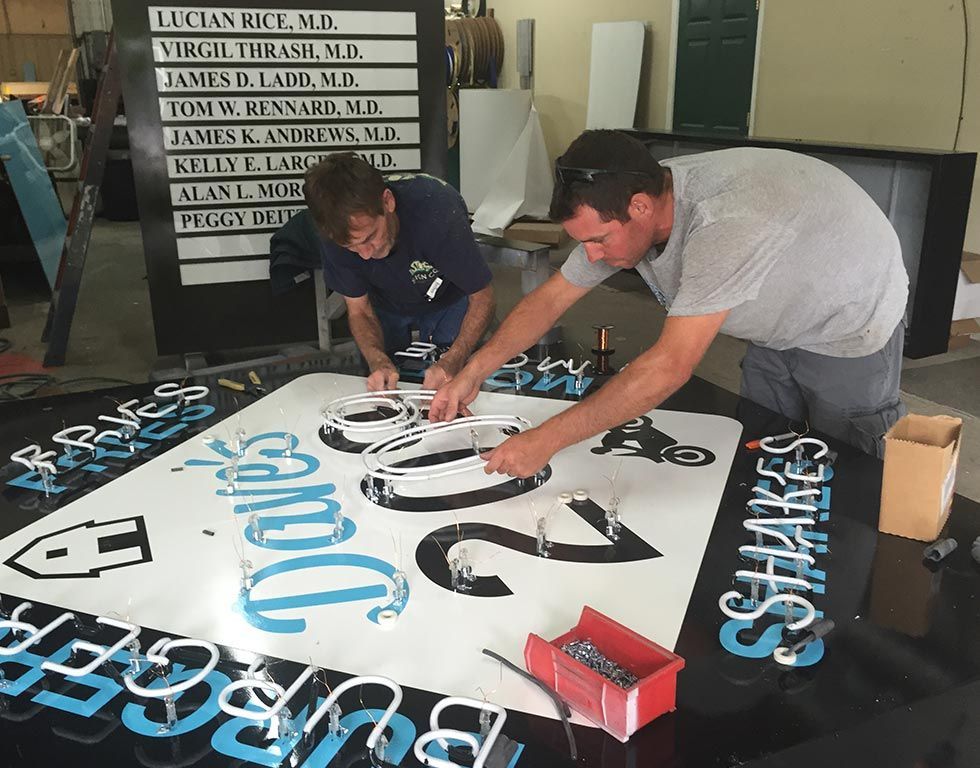 Two men installing neon lights on a sign for 
