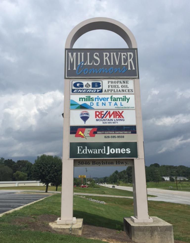 Sign for Mills River Commons shopping center with business logos against a cloudy sky; businesses listed include G&B Energy, Mills River Family Dental, RE/MAX, and Edward Jones.