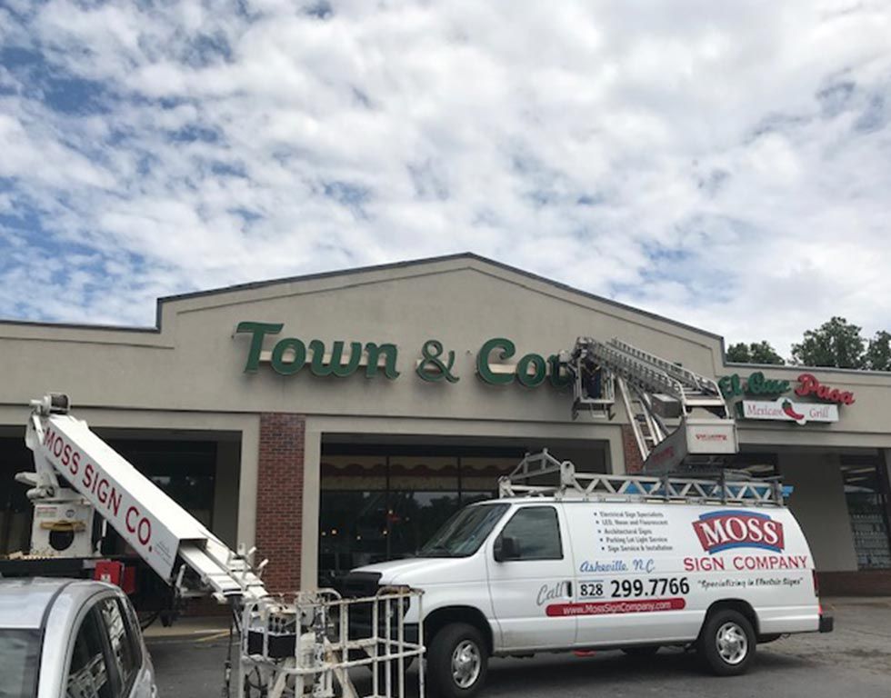 A white van with the Moss Sign Company logo is parked in front of a building with a 