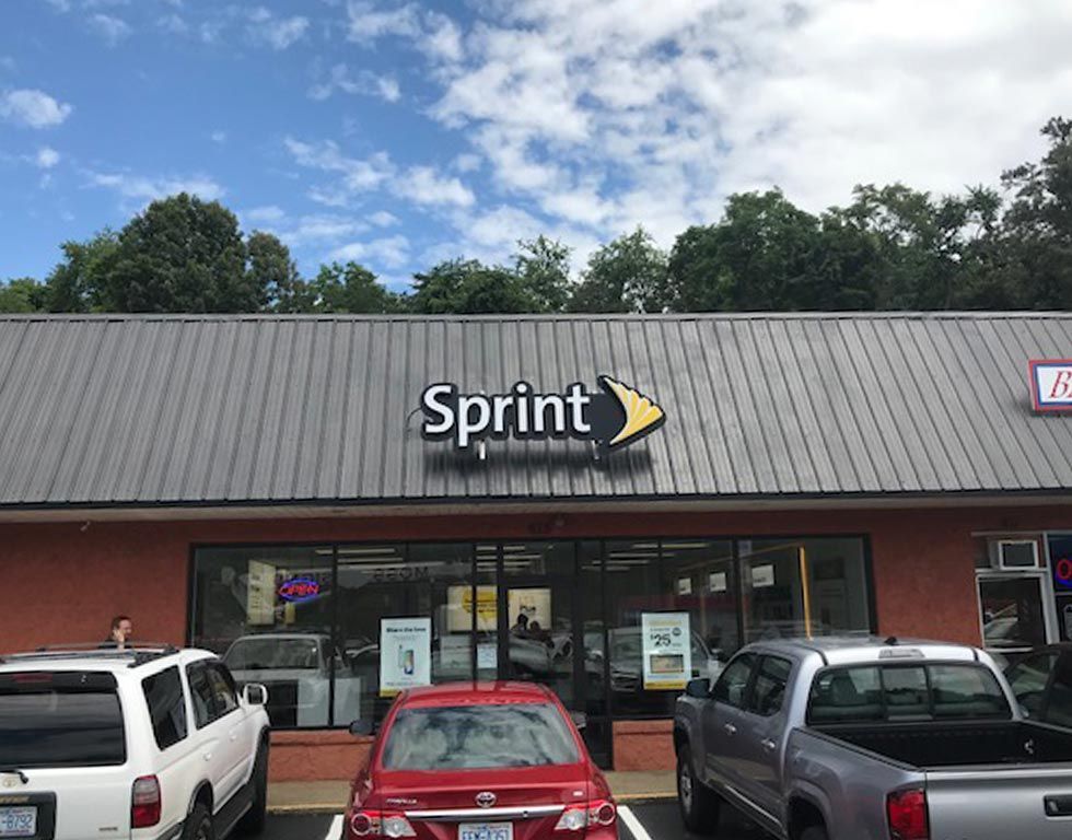 Sprint store front with a gray roof, red brick trim, and cars parked in front under a partly cloudy blue sky.