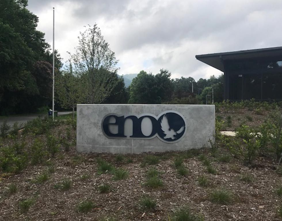 Sign for emoo, a company, with logo, set in front of a building. Concrete sign is dark blue with a white eagle logo.