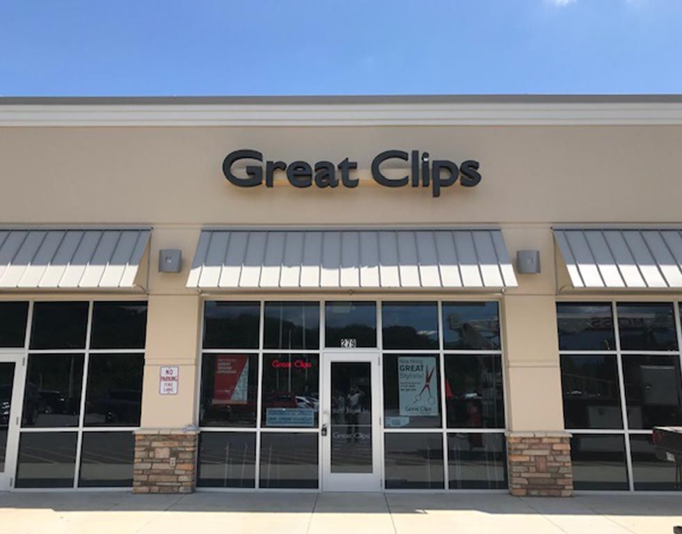 Great Clips storefront with black lettering, tan exterior, and glass windows; blue sky in the background.