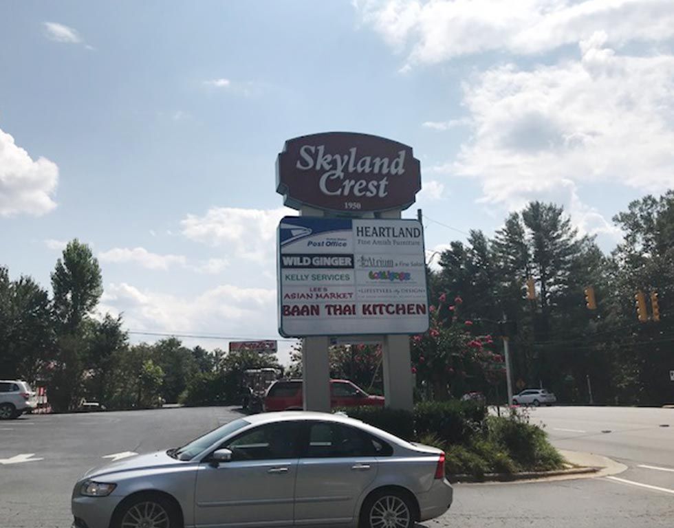 Sign for Skyland Crest shopping center with restaurant names below, car in foreground.