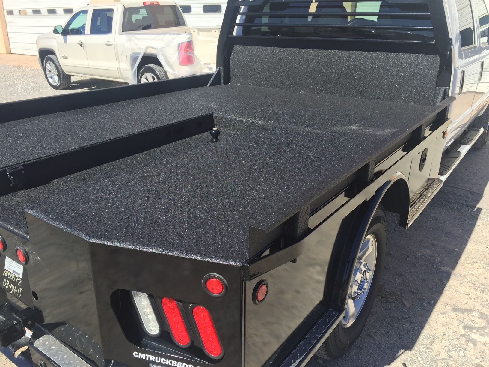 A white truck is parked next to a black truck bed.