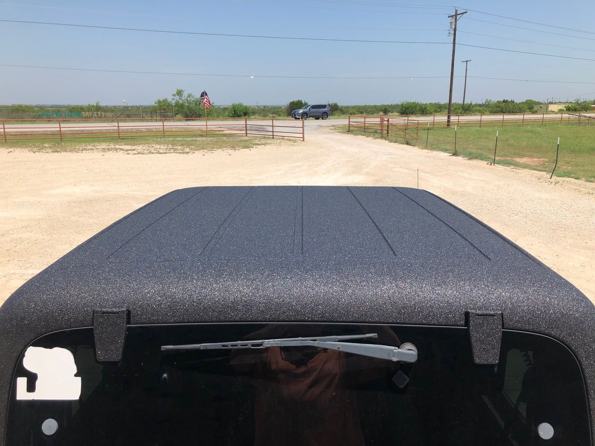 A truck with a black roof is parked on a dirt road.
