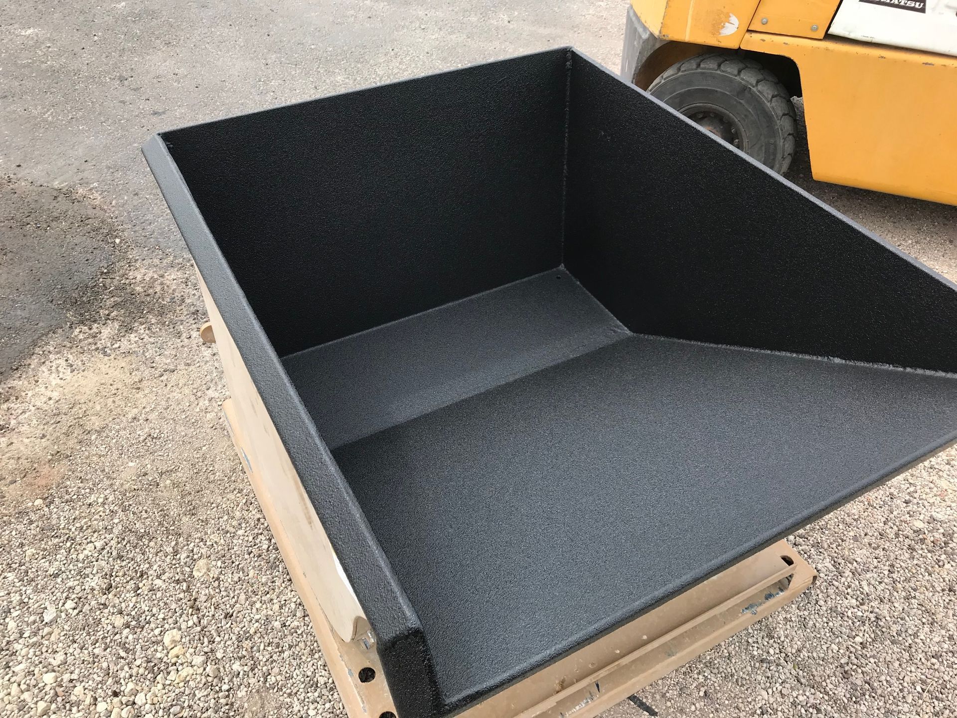 A black container is sitting on a wooden pallet next to a yellow forklift.
