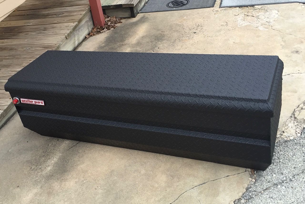 A black toolbox is sitting on the ground next to a wooden deck.