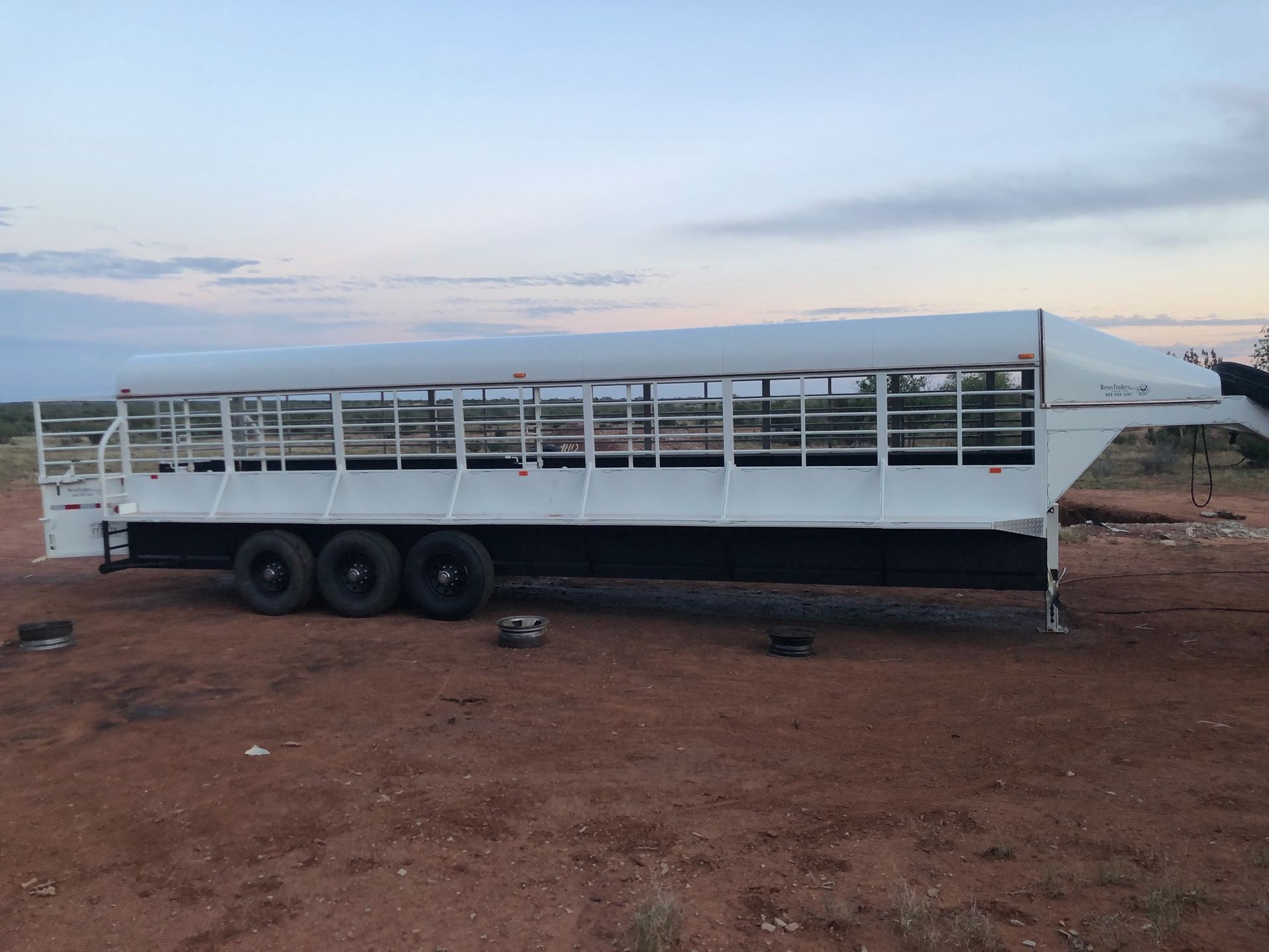 A large white trailer is parked in a dirt field