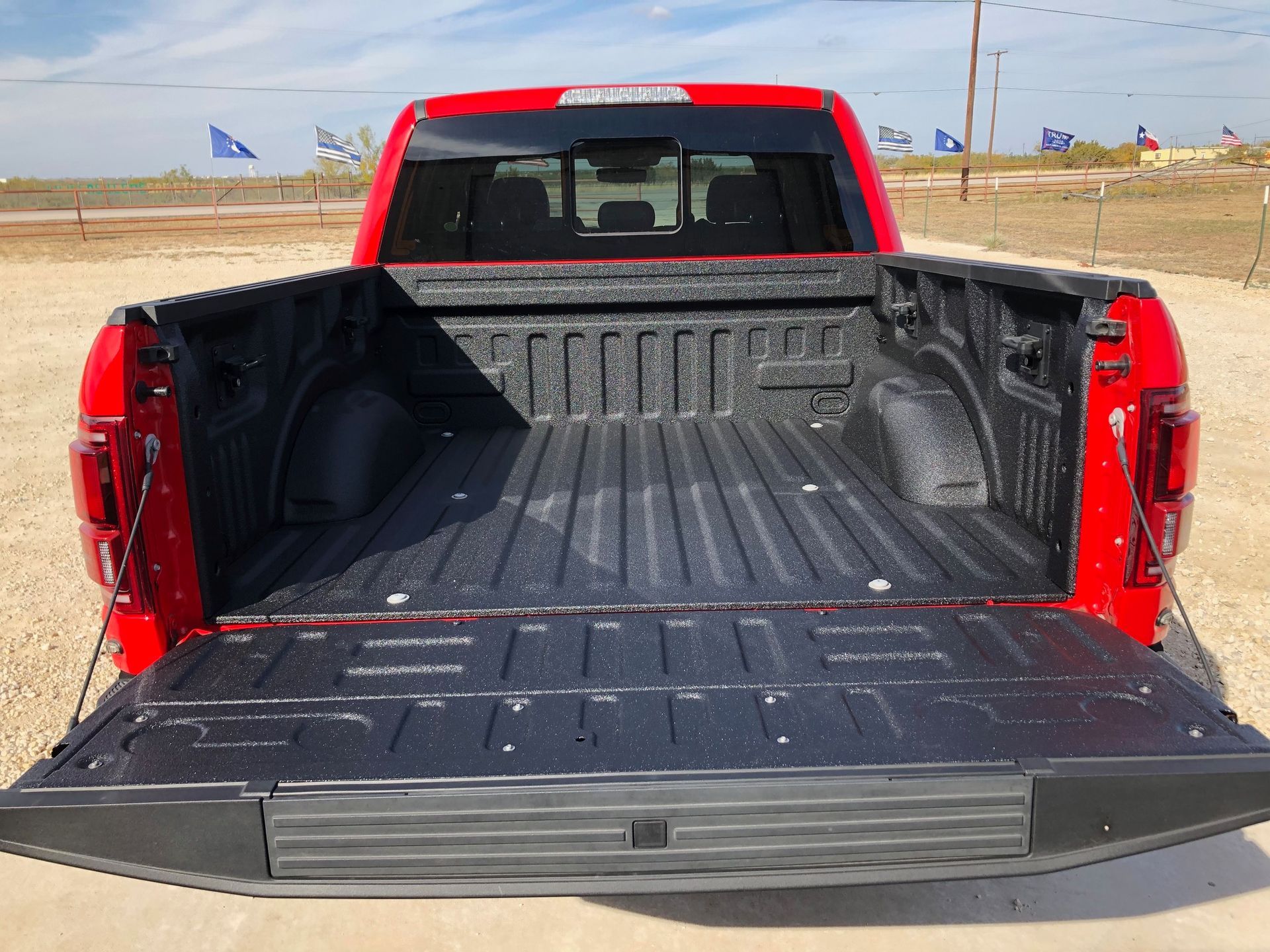 A red truck with the bed open is parked in a dirt field.