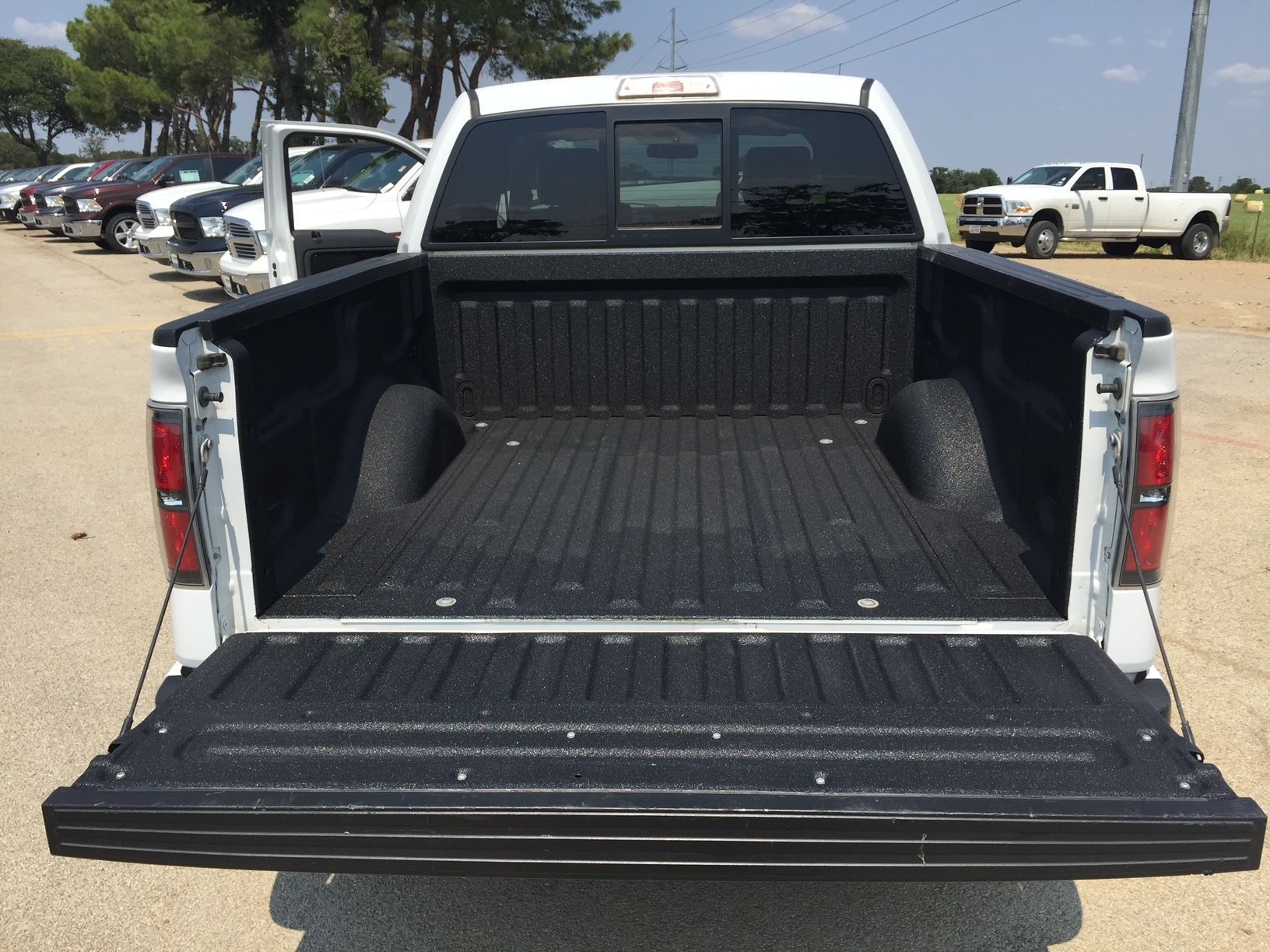 A white truck with the bed open is parked in a parking lot.