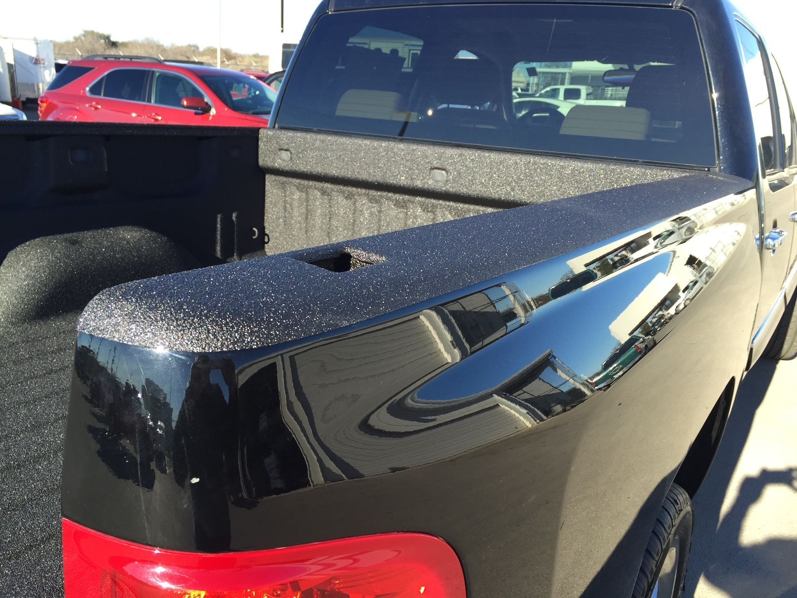 A black truck with a red tail light is parked in a parking lot