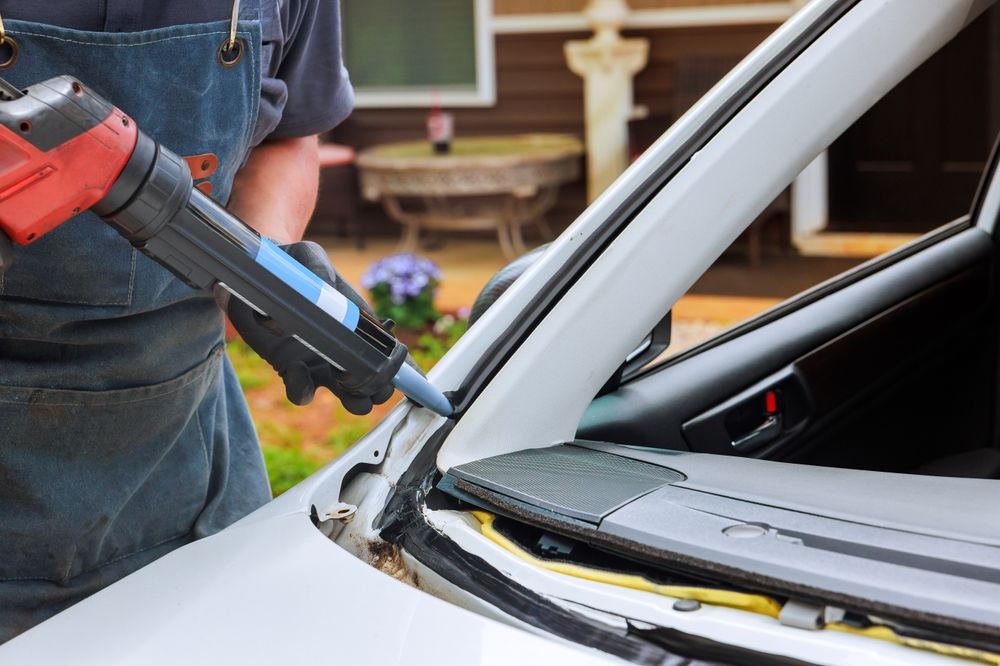 Person applies sealant to a car's windshield frame with a caulking gun.