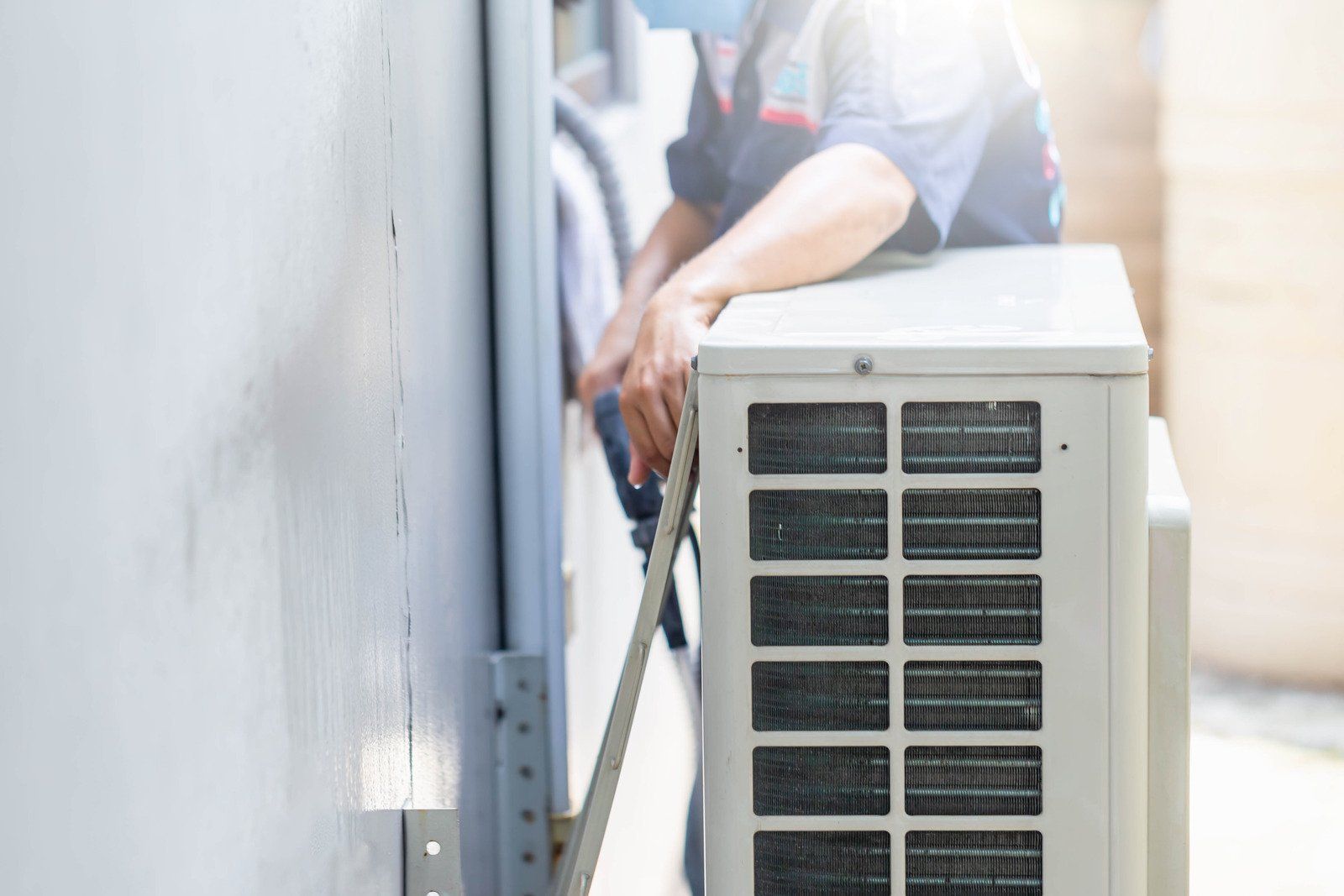 HVAC technician installing an air conditioning unit outside on a wall.