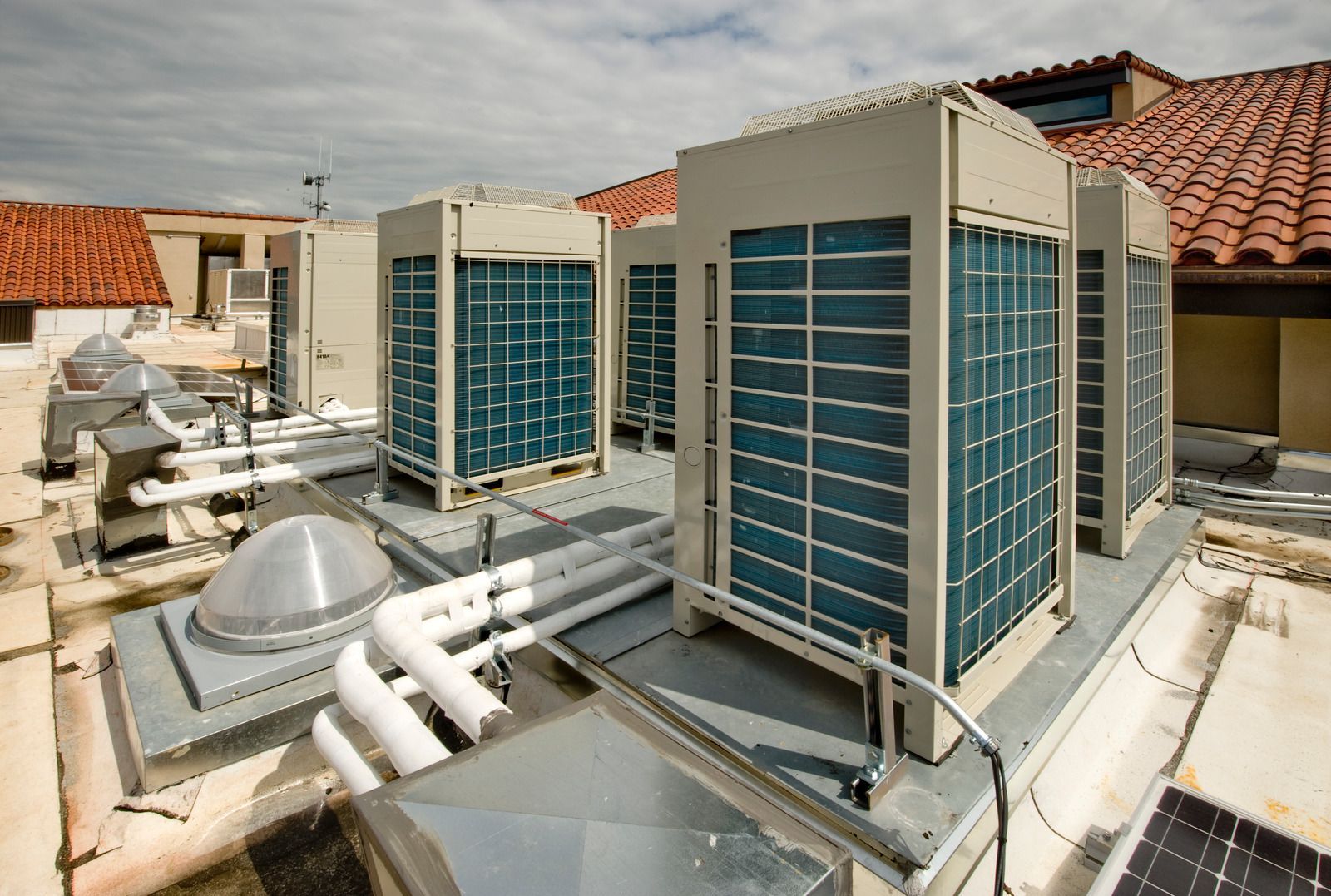 HVAC units on a rooftop, beige metal with blue vents, overlooking terracotta tile roof.