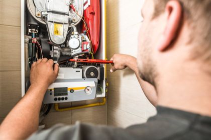 Person using a wrench to repair a wall-mounted boiler.